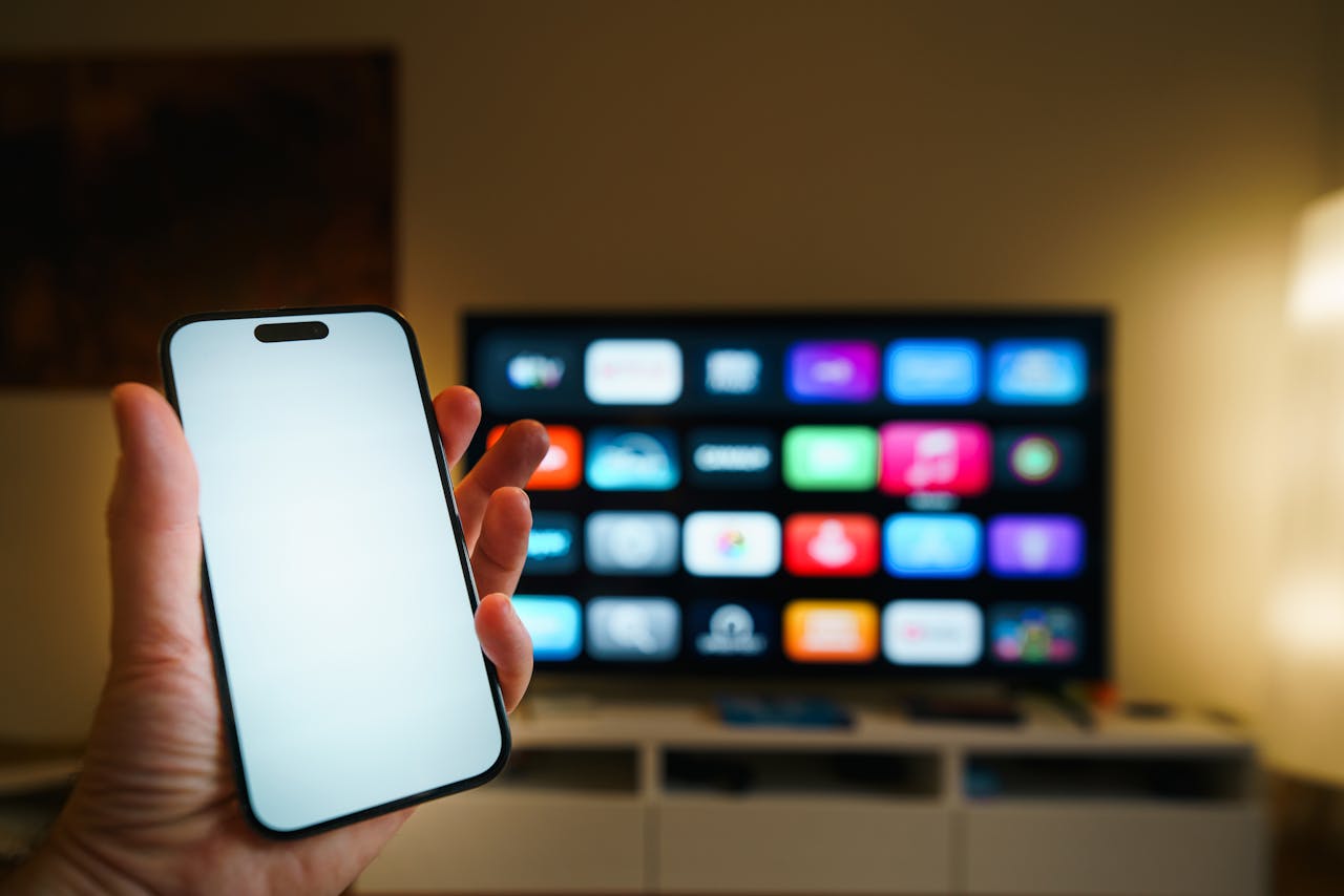 A smartphone in focus with a smart TV displaying apps in a cozy living room.